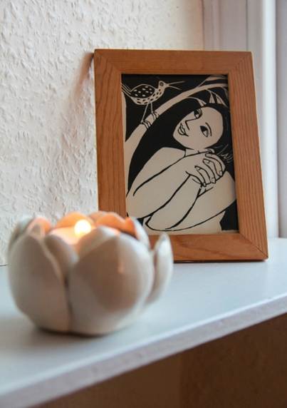 candle in front of picture in frame of woman looking at a bird